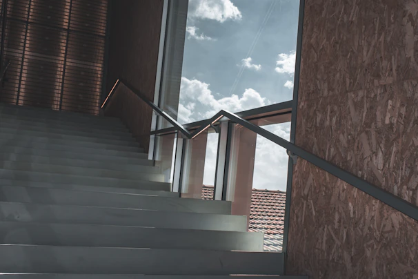 A sculptural staircase framed by large windows revealing textured natural materials and warm hues.