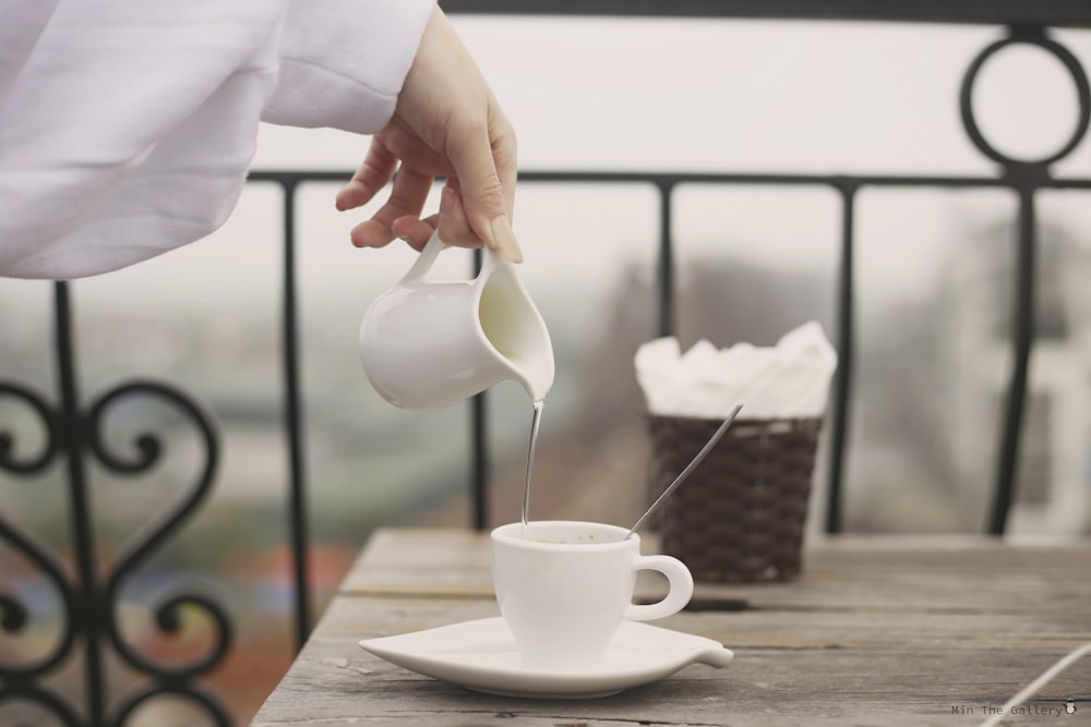 person pouring white ceramic teacup on white ceramic saucer
