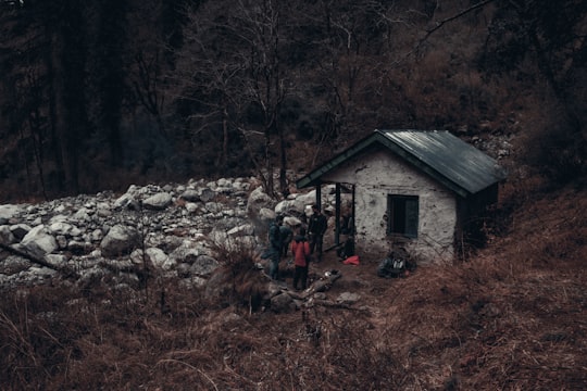 man in black jacket standing near brown wooden house during daytime in Great Himalayan National Park India