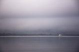 Minimalist seascape with a lone sailboat on calm water.