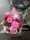 A colorful bouquet of pink flowers, including gerberas and roses, is placed on the back of a bicycle with a pink bag. The flowers are wrapped in clear cellophane and the bike is parked on a wet brick pavement.