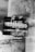 A black and white photo of a weathered poster on a textured wall. The poster contains several German words in bold, overlapping text, some of which are obscured. The background shows a gritty texture with signs of wear and tear.