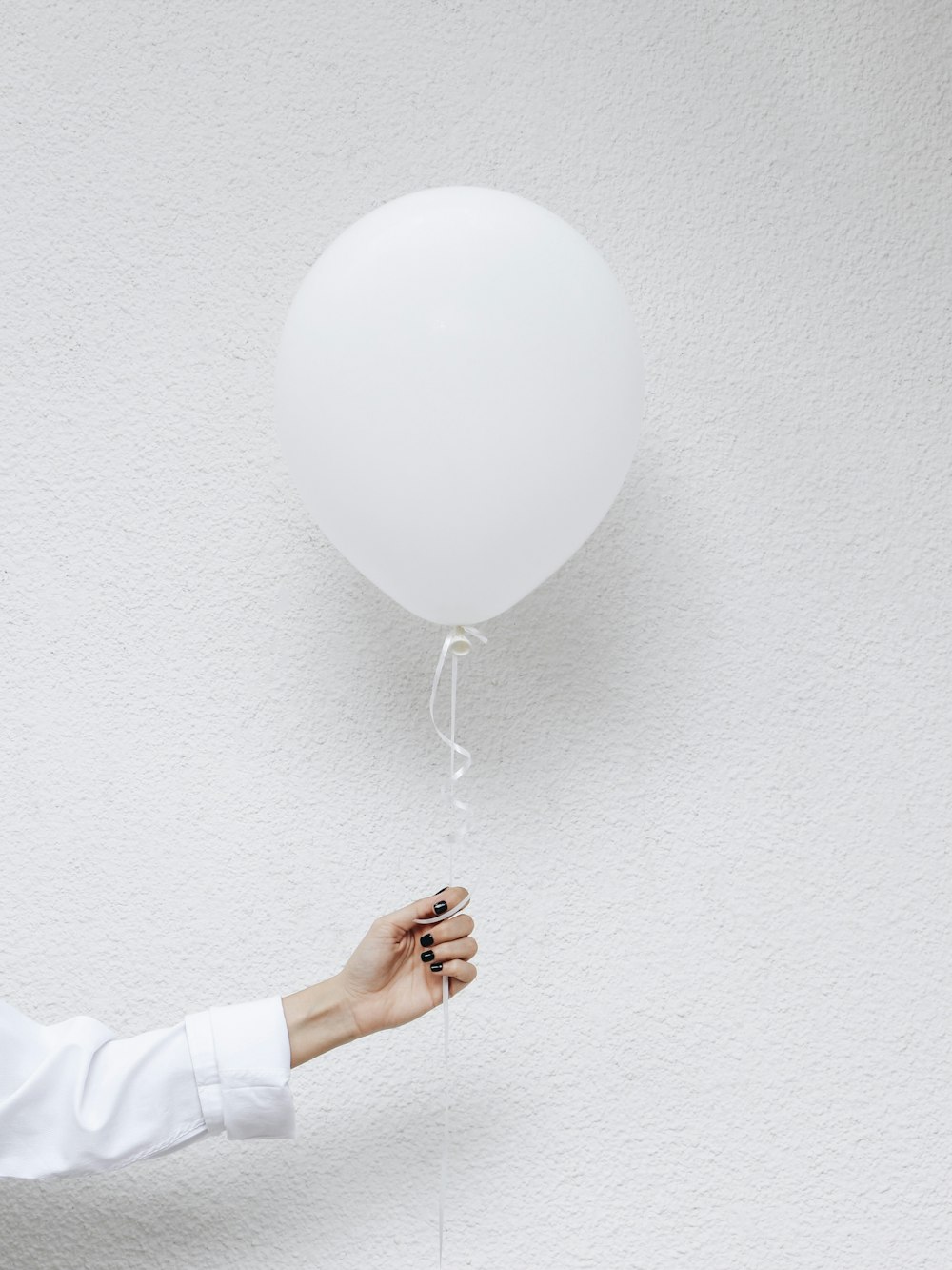 Persona che tiene i palloncini bianchi vicino al muro bianco