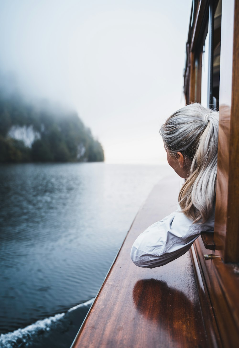 Frau im weißen Hemd sitzt tagsüber auf braunem Holzboot