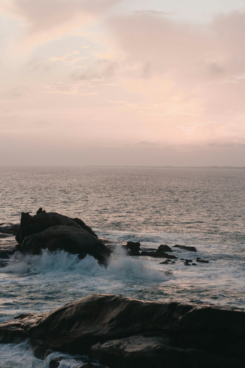 ocean waves crashing on rocks under white clouds during daytime