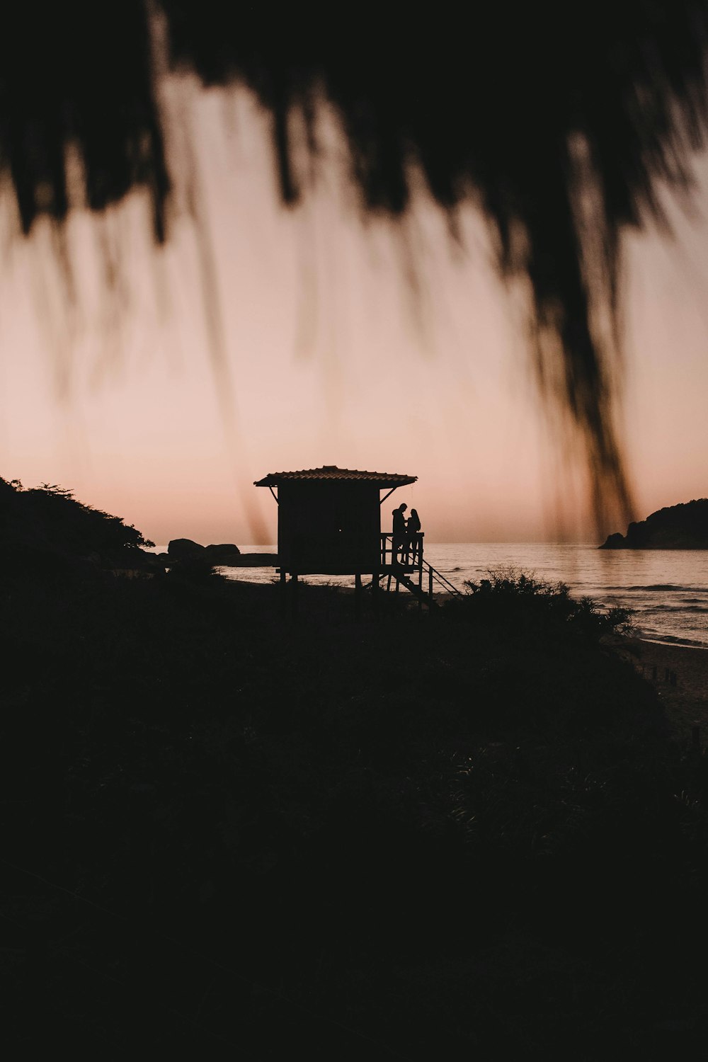 silhouette of person standing on rock near body of water