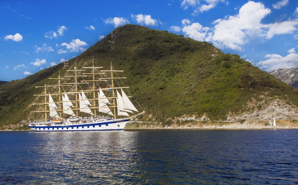 white and blue boat on water near green mountain under blue sky during daytime