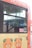 A portion of a bus with an orange color on its upper section, featuring cartoon depictions of a bear with leaf-shaped ears on its lower part. The bus displays the name IYOTETSU at the top. A window shows reflections and a leafy plant is visible through the glass. There are stickers with Japanese text on the side of the bus.