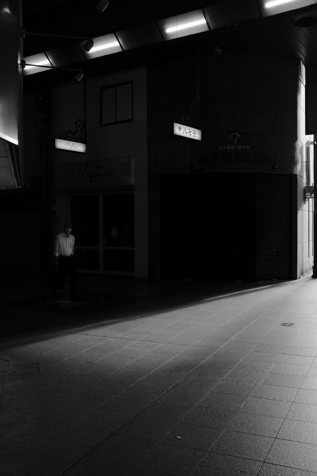 grayscale photo of man walking on sidewalk