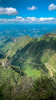 A scenic mountain road winding through lush green forests under a bright blue sky.