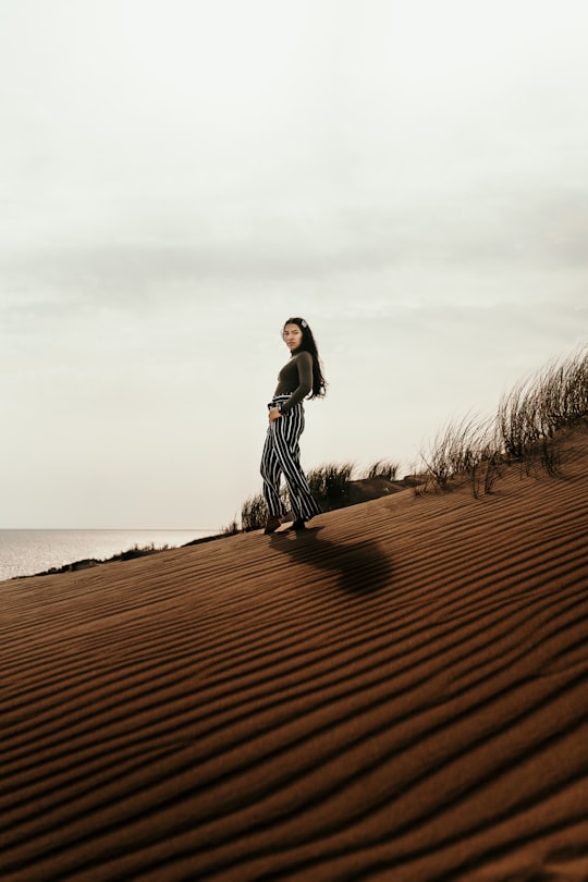 woman in black dress standing on brown sand near body of water during daytime in Nida Lithuania