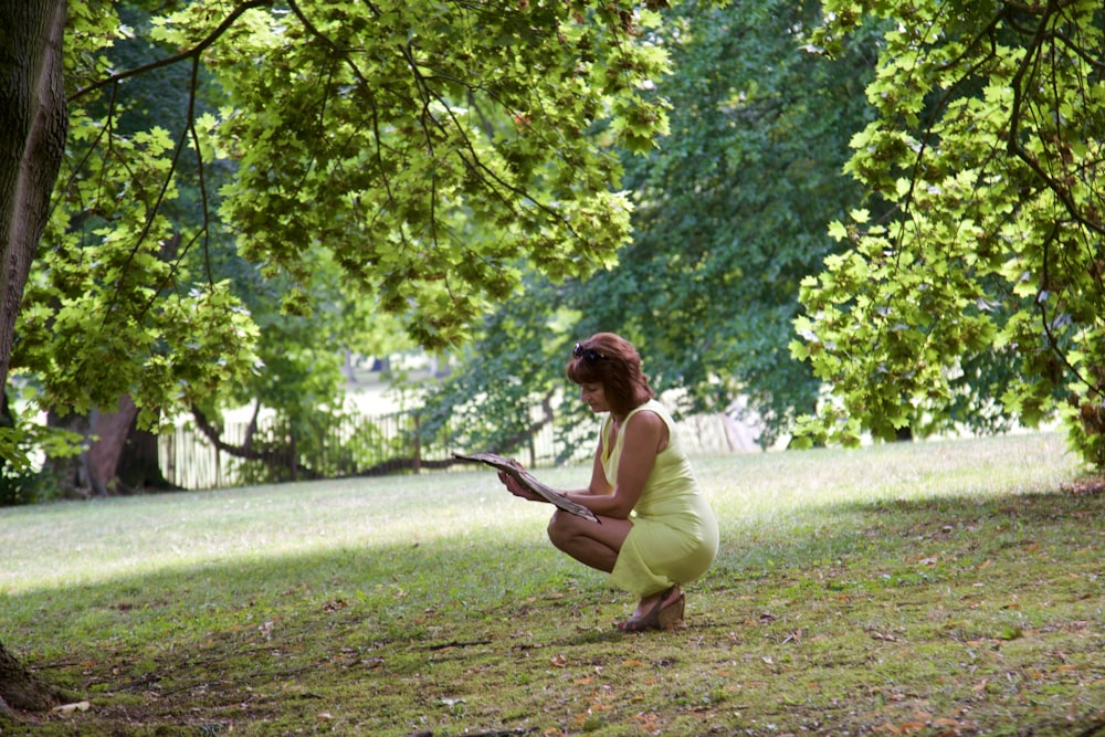 a woman in a yellow dress crouches in the grass