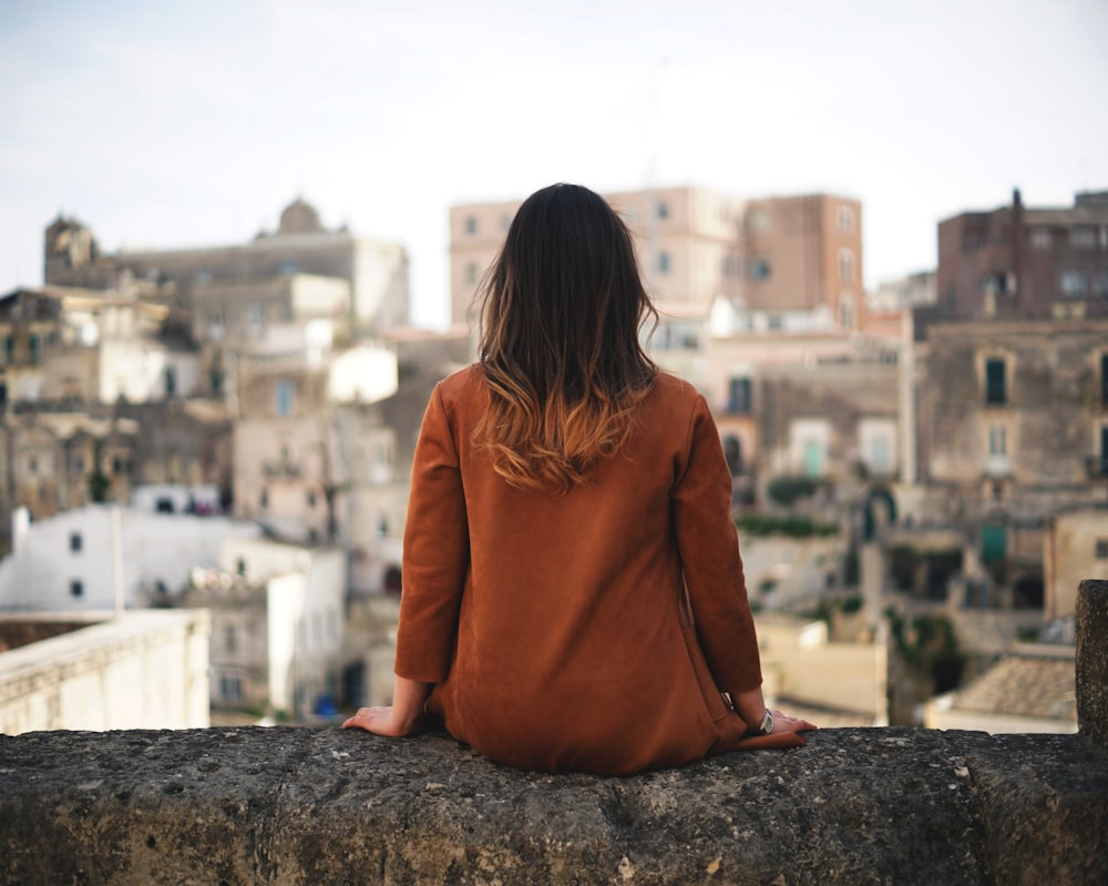 Donna in camicia a maniche lunghe marrone che si siede sulla roccia grigia durante il giorno