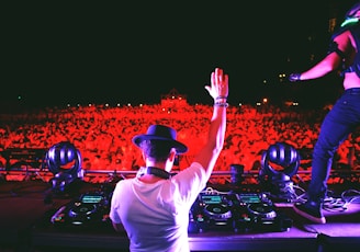 man in white t-shirt and black cap standing in front of dj controller