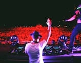 man in white t-shirt and black cap standing in front of dj controller