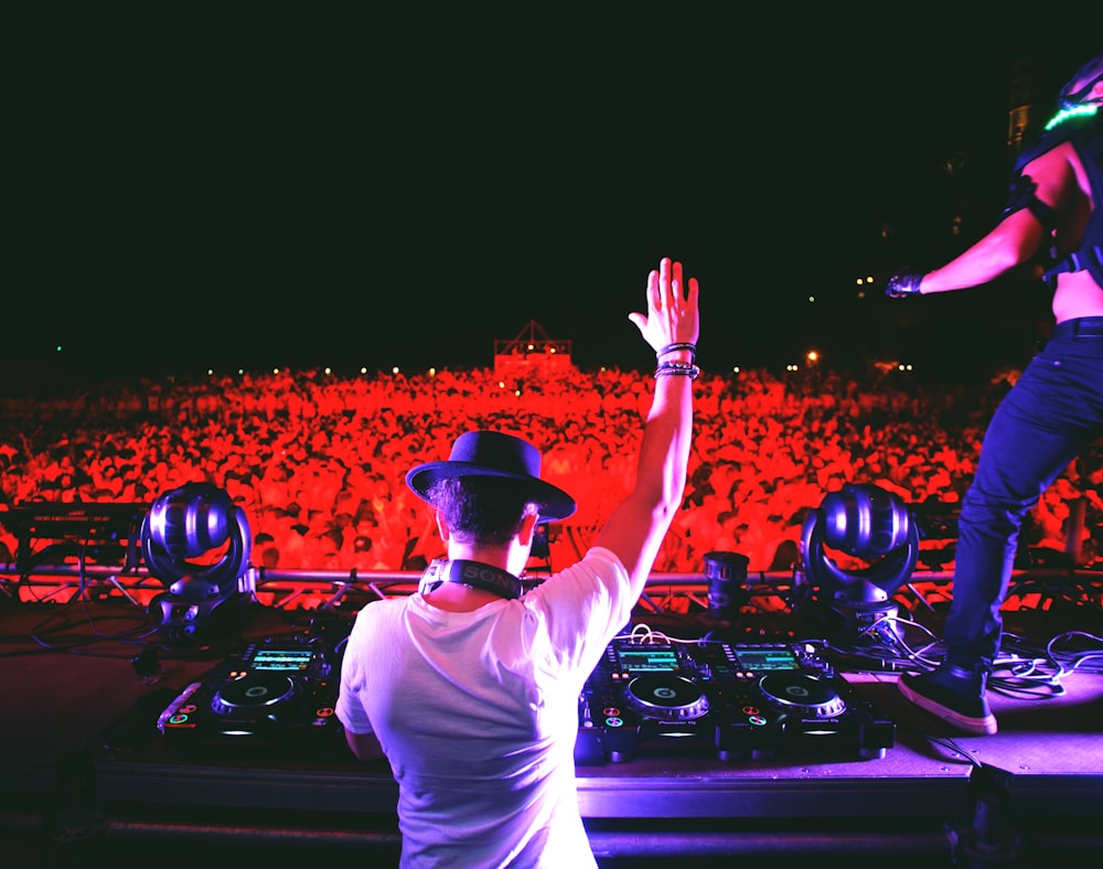 man in white t-shirt and black cap standing in front of dj controller