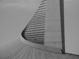 A modern architectural structure with a curved design featuring a series of horizontal lines and panels. The sleek and minimalistic form suggests an innovative architectural style.