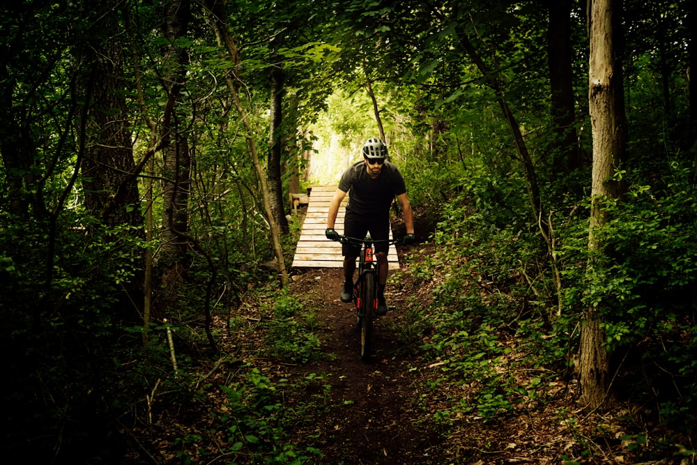 uomo in giacca nera che cavalca la bicicletta sul ponte di legno marrone