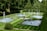 A beautifully manicured garden featuring multiple rectangular and circular water fountains, surrounded by neatly trimmed green lawns and dense trees. The water jets rise gracefully from the fountains, creating a serene and elegant atmosphere.