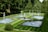 A beautifully manicured garden featuring multiple rectangular and circular water fountains, surrounded by neatly trimmed green lawns and dense trees. The water jets rise gracefully from the fountains, creating a serene and elegant atmosphere.