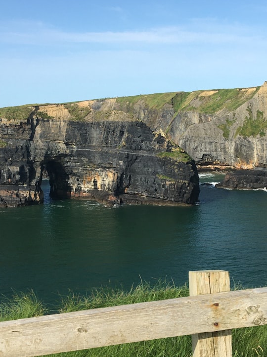 brown wooden dock on green body of water near brown and green mountain during daytime in Ballybunion Ireland