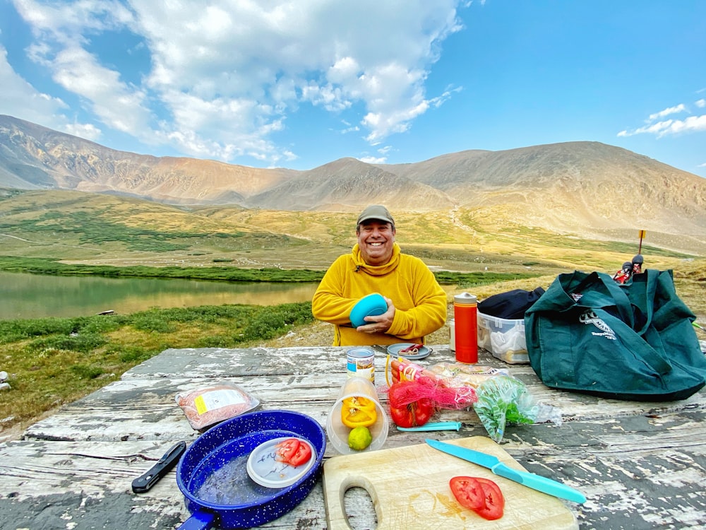 uomo in maglietta girocollo gialla che si siede a terra vicino alla montagna durante il giorno