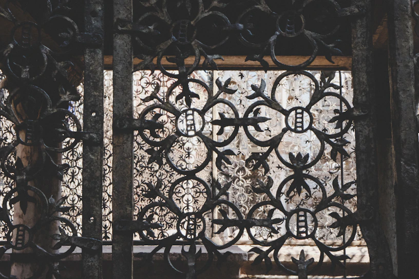 Close-up of a handcrafted wrought iron window frame with intricate floral patterns against a dark background.