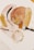 A collection of art supplies including two paintbrushes, a glass container with gold leaf fragments, and abstract art featuring soft colors and gold textures. The design includes overlapping ovals and circular patterns with shiny elements.