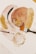 A collection of art supplies including two paintbrushes, a glass container with gold leaf fragments, and abstract art featuring soft colors and gold textures. The design includes overlapping ovals and circular patterns with shiny elements.