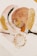 A collection of art supplies including two paintbrushes, a glass container with gold leaf fragments, and abstract art featuring soft colors and gold textures. The design includes overlapping ovals and circular patterns with shiny elements.