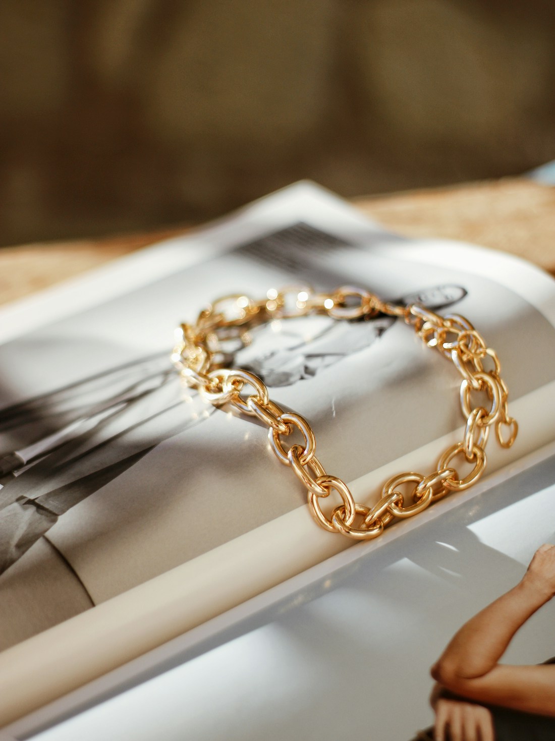 Hand-finished gold paperclip-link bracelet resting on a magazine