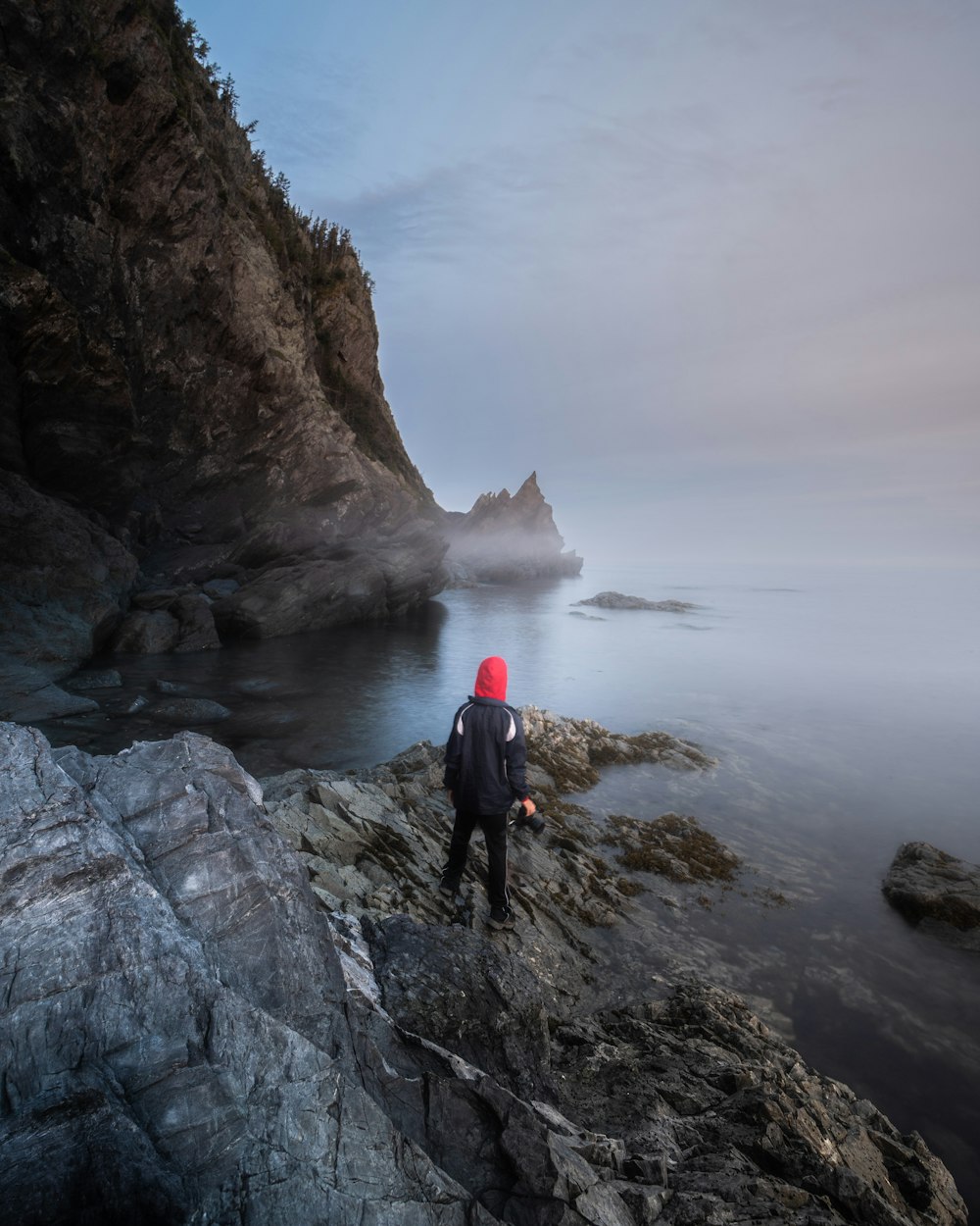 person in black jacket standing on rock formation near body of water during daytime