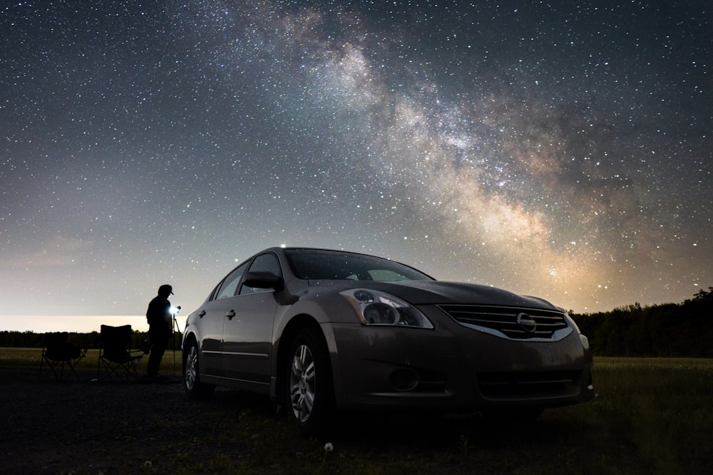 2 hombres de pie junto a un coche negro bajo la noche estrellada