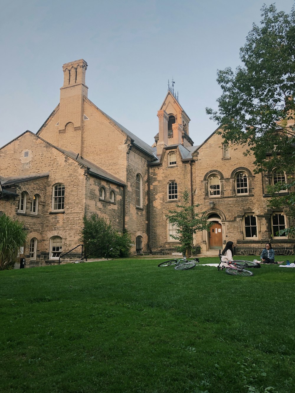 woman in white shirt sitting on green grass field near brown concrete building during daytime