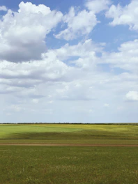 A wide open green field with rolling hills near Luque, showcasing potential land for development under a clear blue sky.