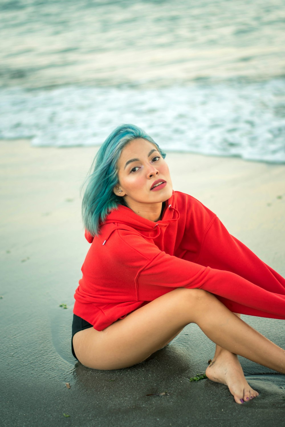 woman in red hoodie and black shorts sitting on beach sand