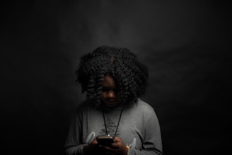 woman in gray long sleeve shirt holding black smartphone checking for messages from her man