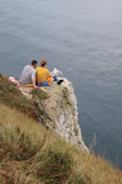 Friends sharing a picnic on a cliff overlooking a sparkling blue sea.