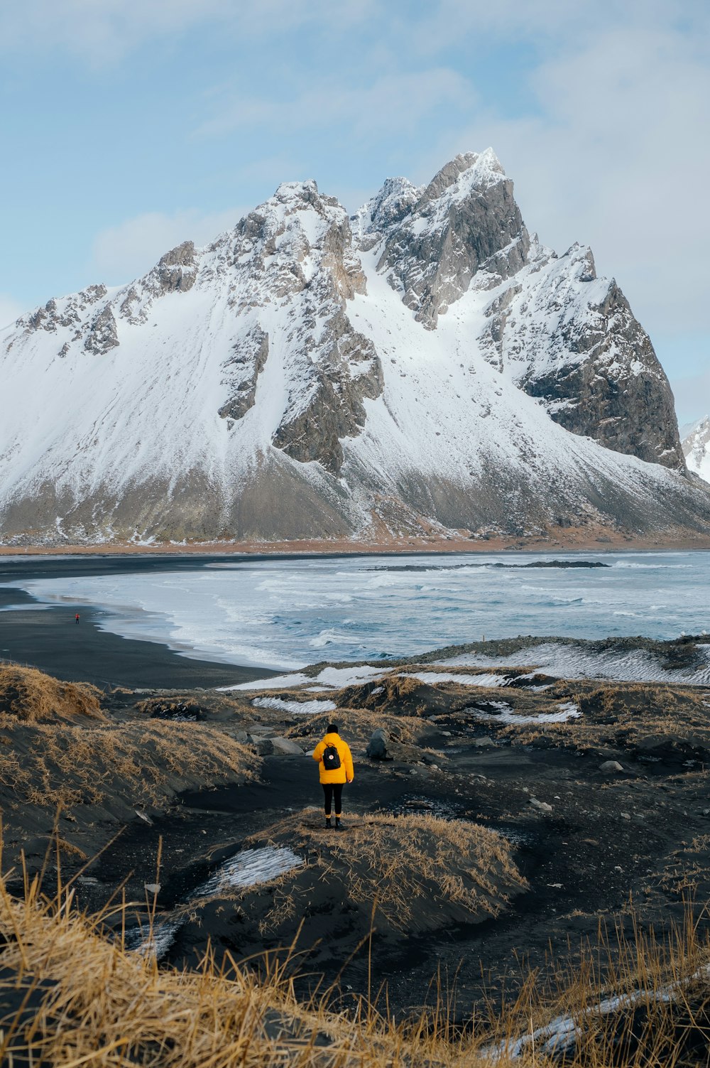 person in yellow jacket standing on brown rock near snow covered mountain during daytime