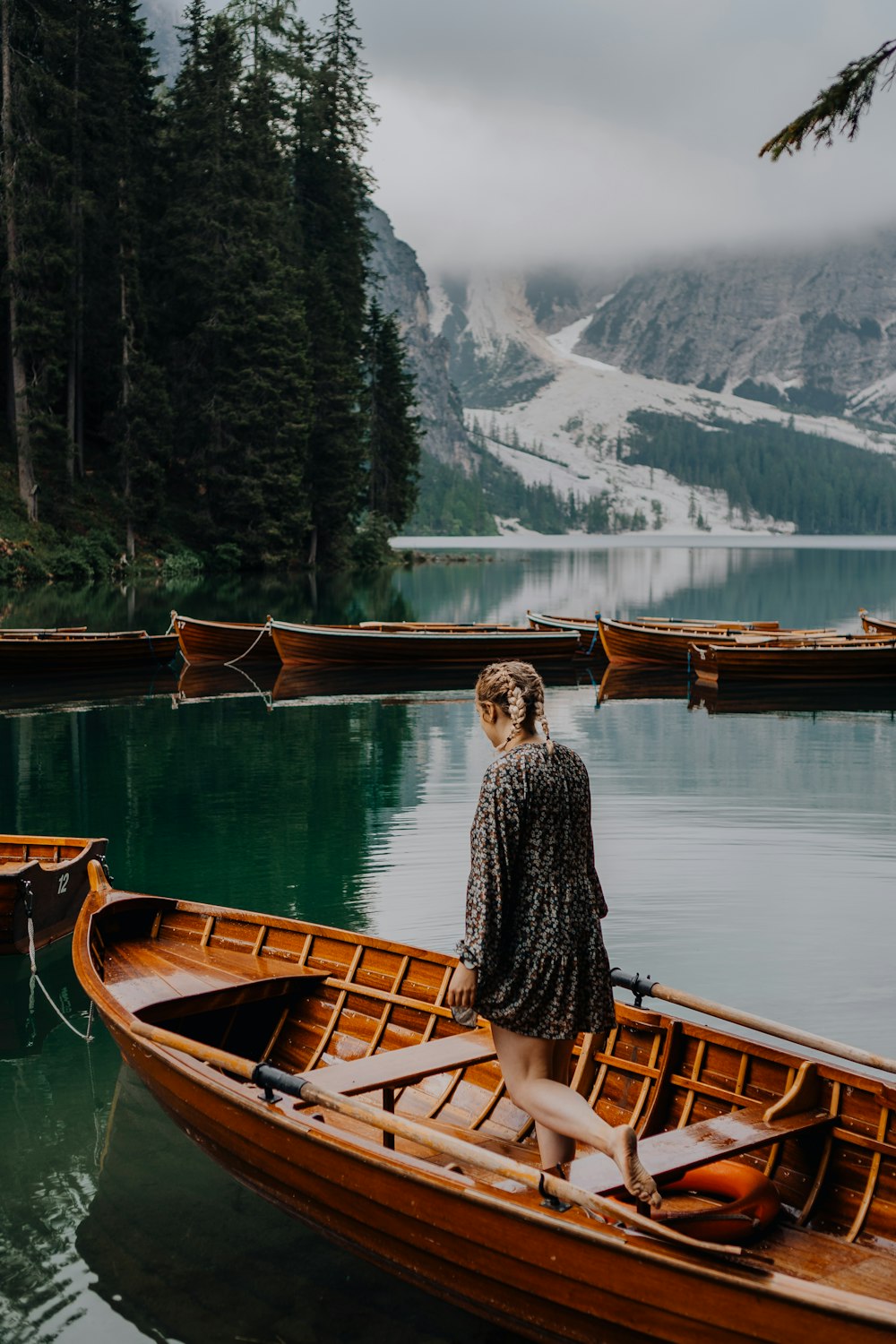 woman in black and white long sleeve shirt sitting on brown wooden boat on lake during