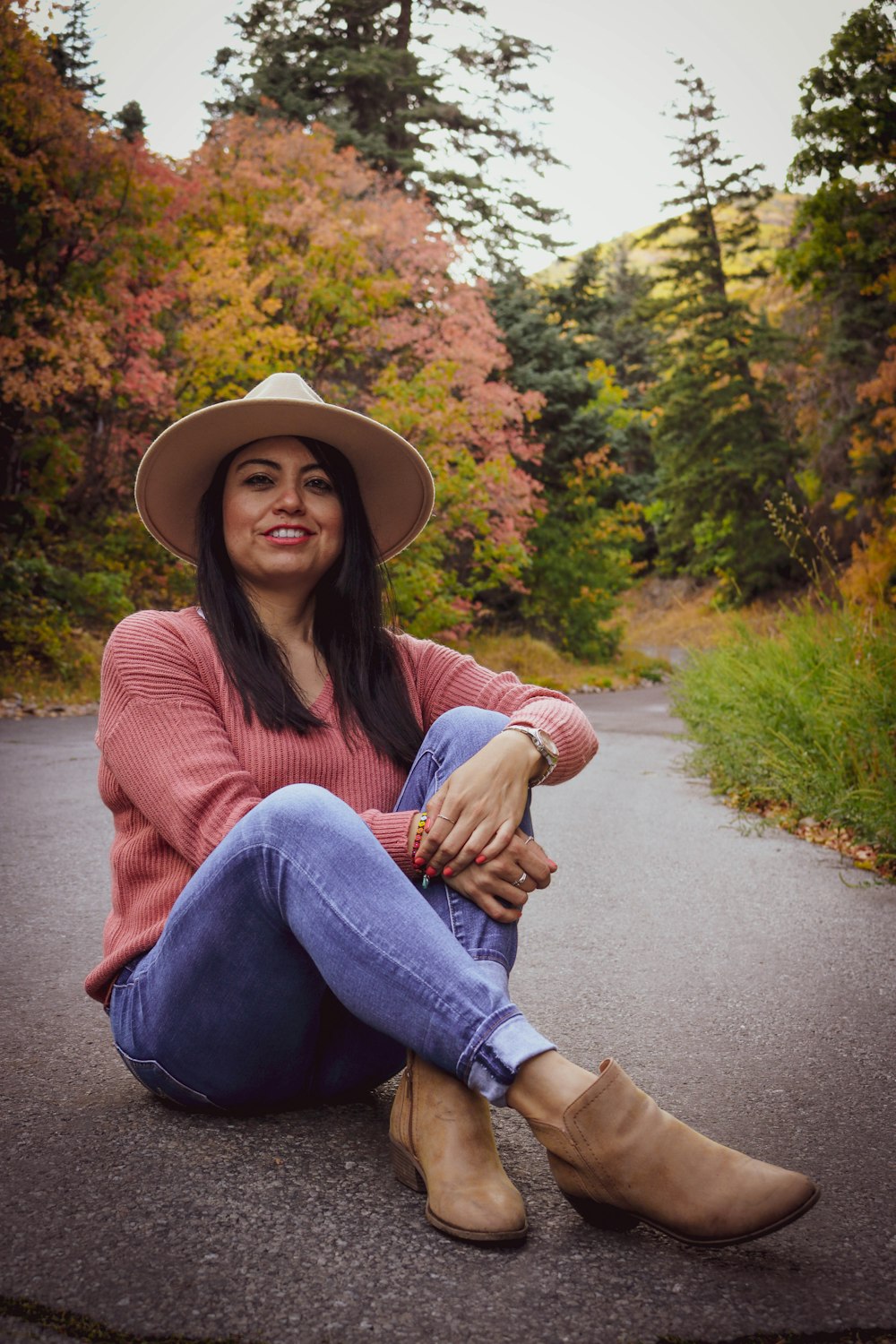woman in red sweater and blue denim jeans sitting on road during daytime