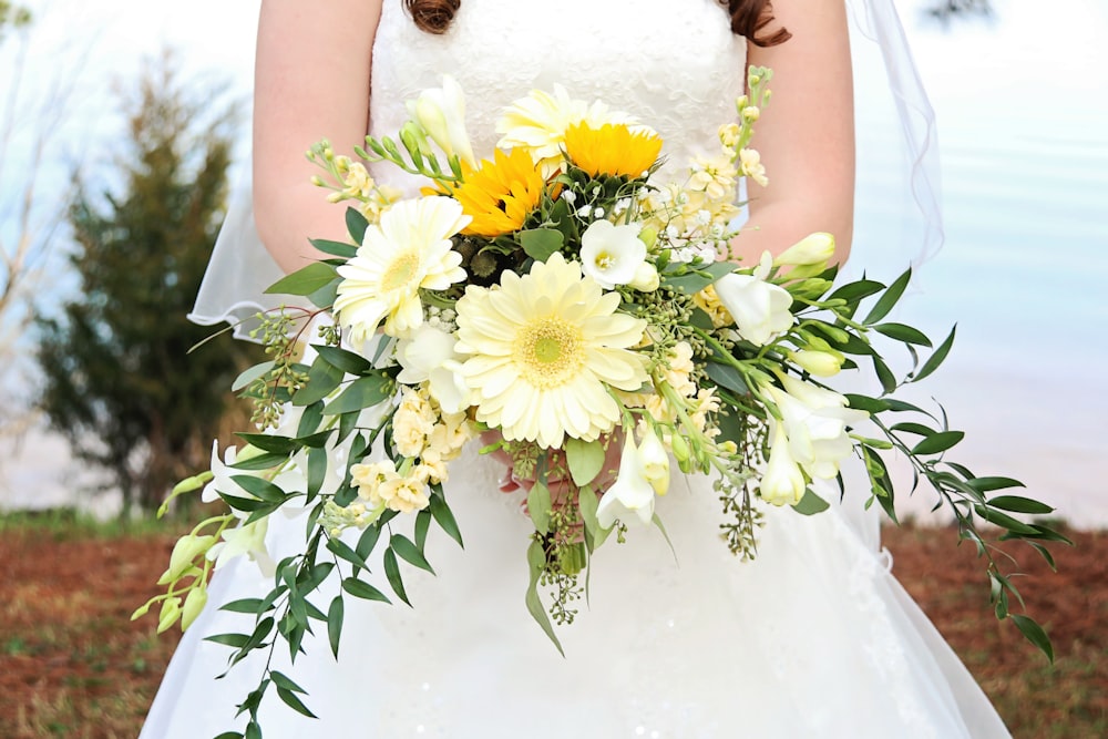 woman in white wedding dress holding white and yellow flowers