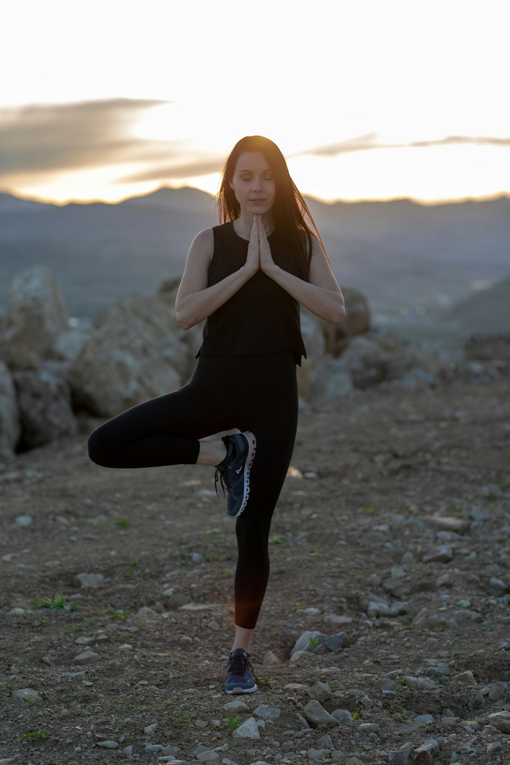 woman in black tank top and black pants standing on rocky shore during sunset