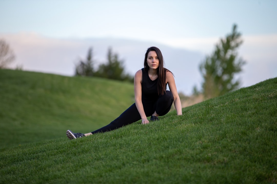 woman in black tank top and black pants sitting on green grass field during daytime