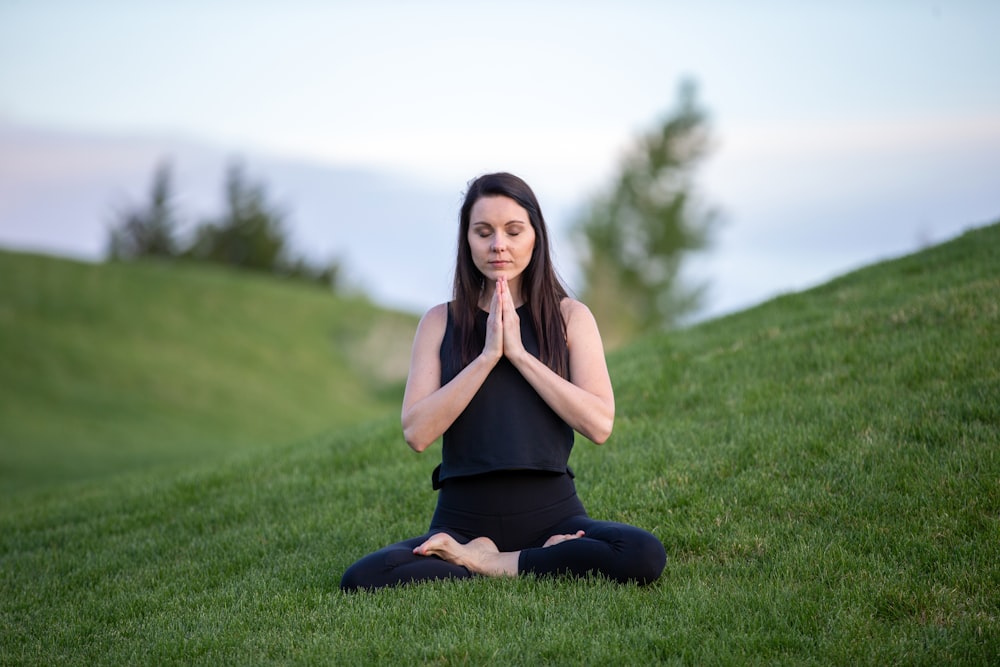 femme en débardeur noir et pantalon noir assis sur un champ d'herbe verte pendant la journée