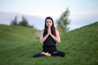 woman in black tank top and black pants sitting on green grass field during daytime