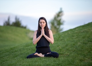 woman in black tank top and black pants sitting on green grass field during daytime