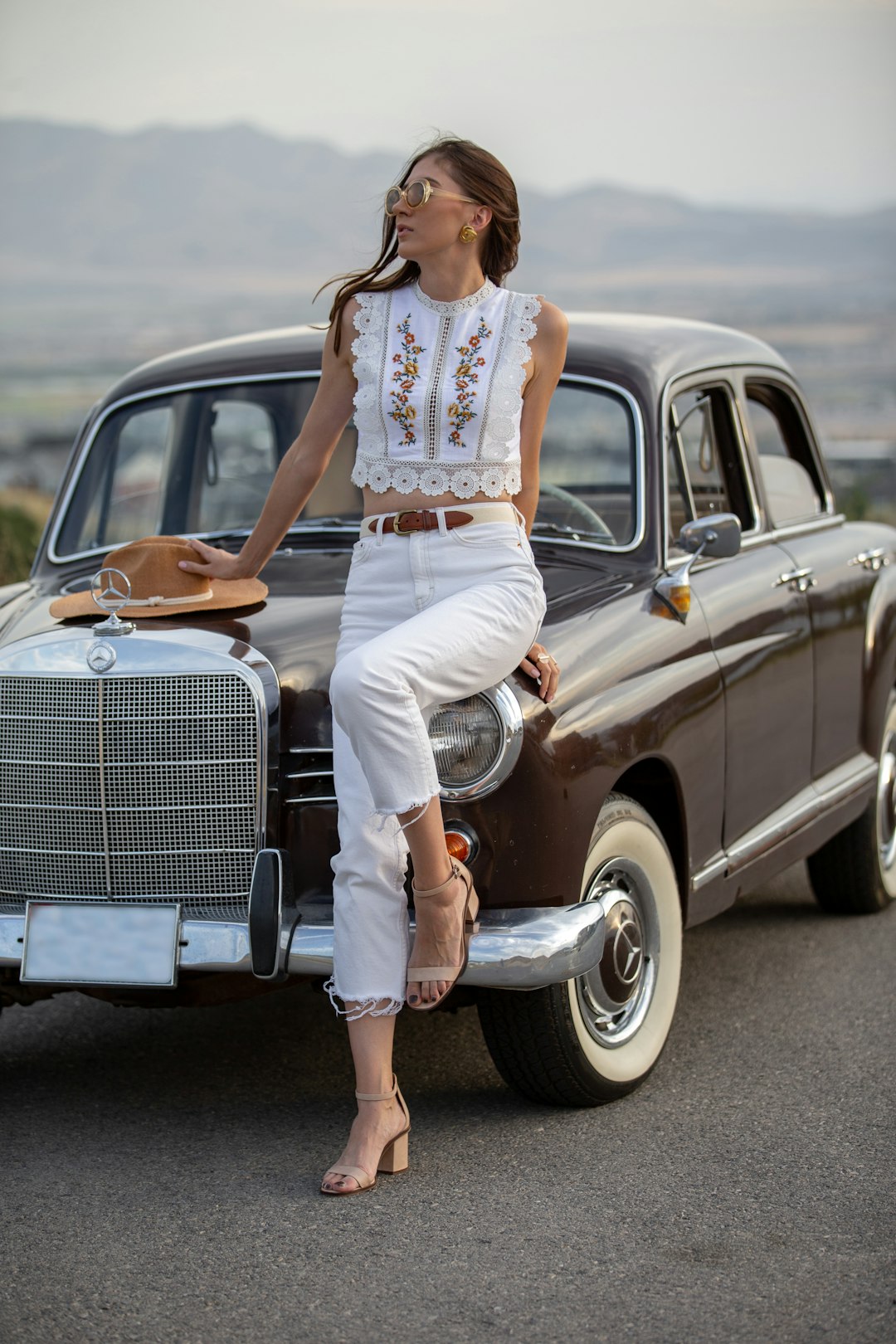 woman in white tank top and white pants leaning on vintage car