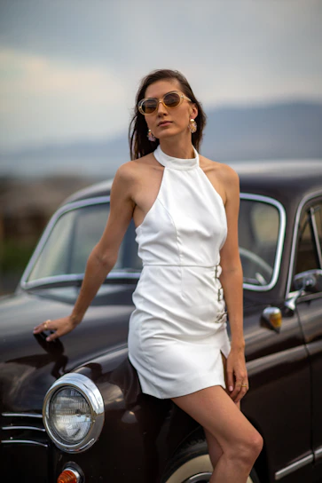 A chic young woman in a silk slip dress stepping out of a vintage car at twilight.