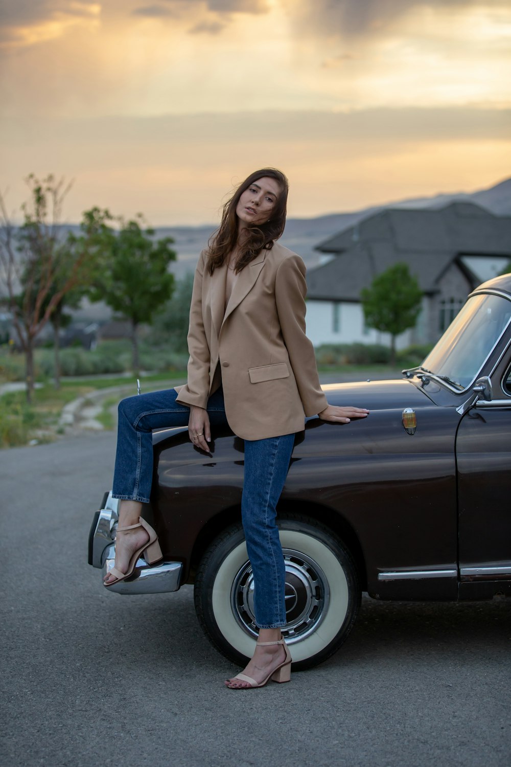 woman in brown coat and blue denim jeans standing beside black car during daytime